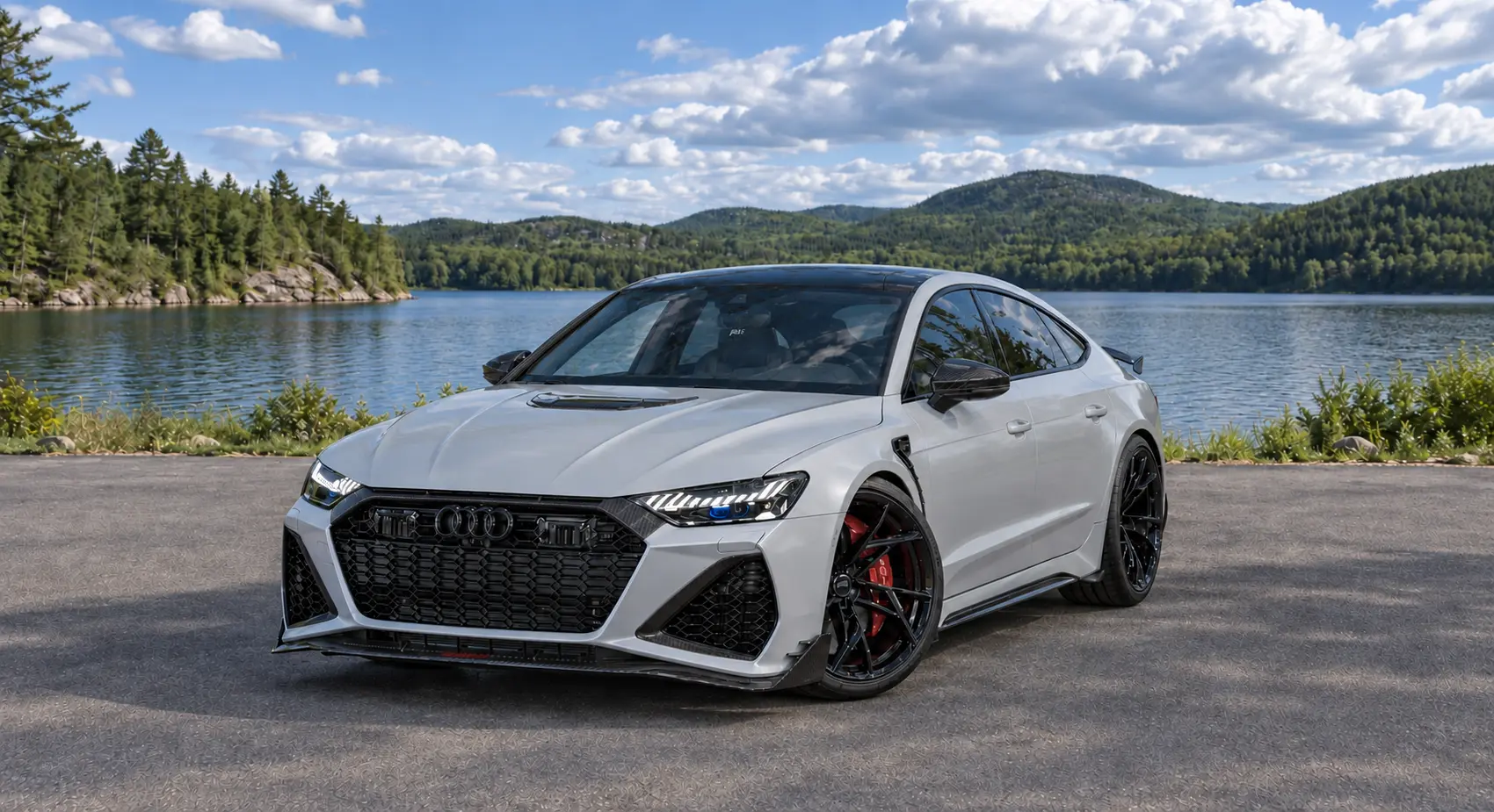 Graues viertüriges Performance-Coupé an einem Seeufer, umgeben von Wald